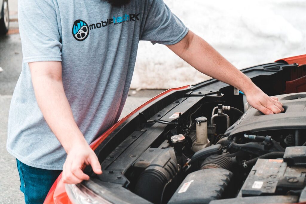 A person checking under the hood of a car to troubleshoot a dead battery assistance issue.